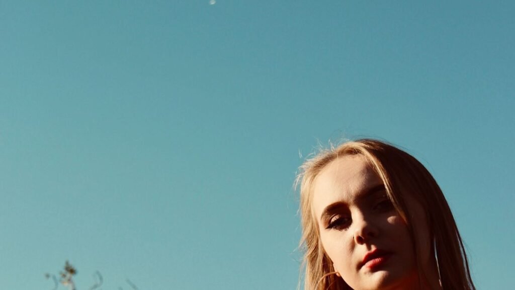 Confident woman posing outdoors in warm sunlight against a blue sky
