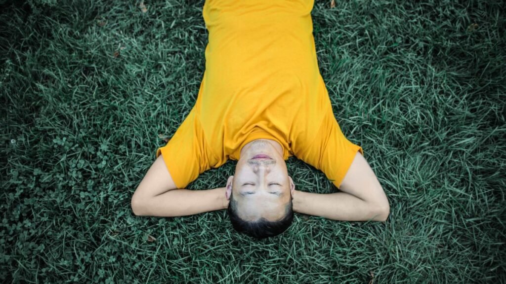A man in a yellow shirt relaxing peacefully on green grass