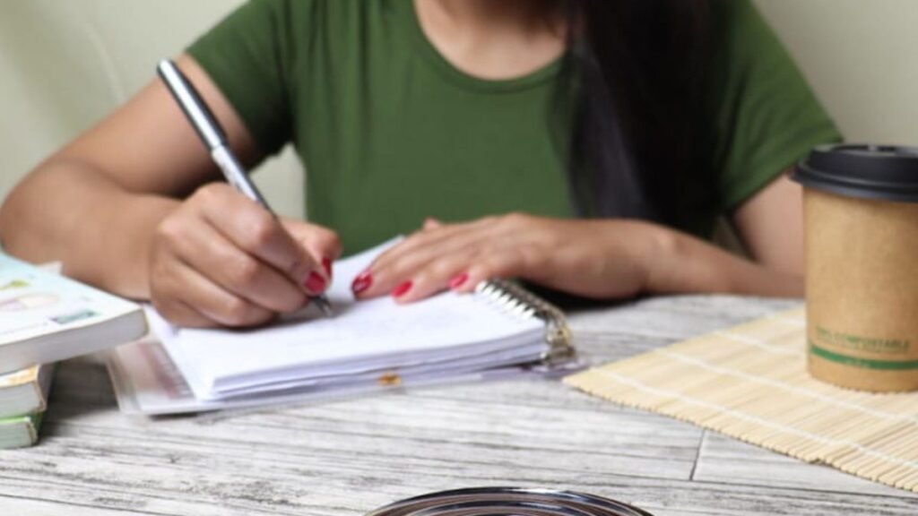 Woman focused, writing in a notebook at her desk with coffee