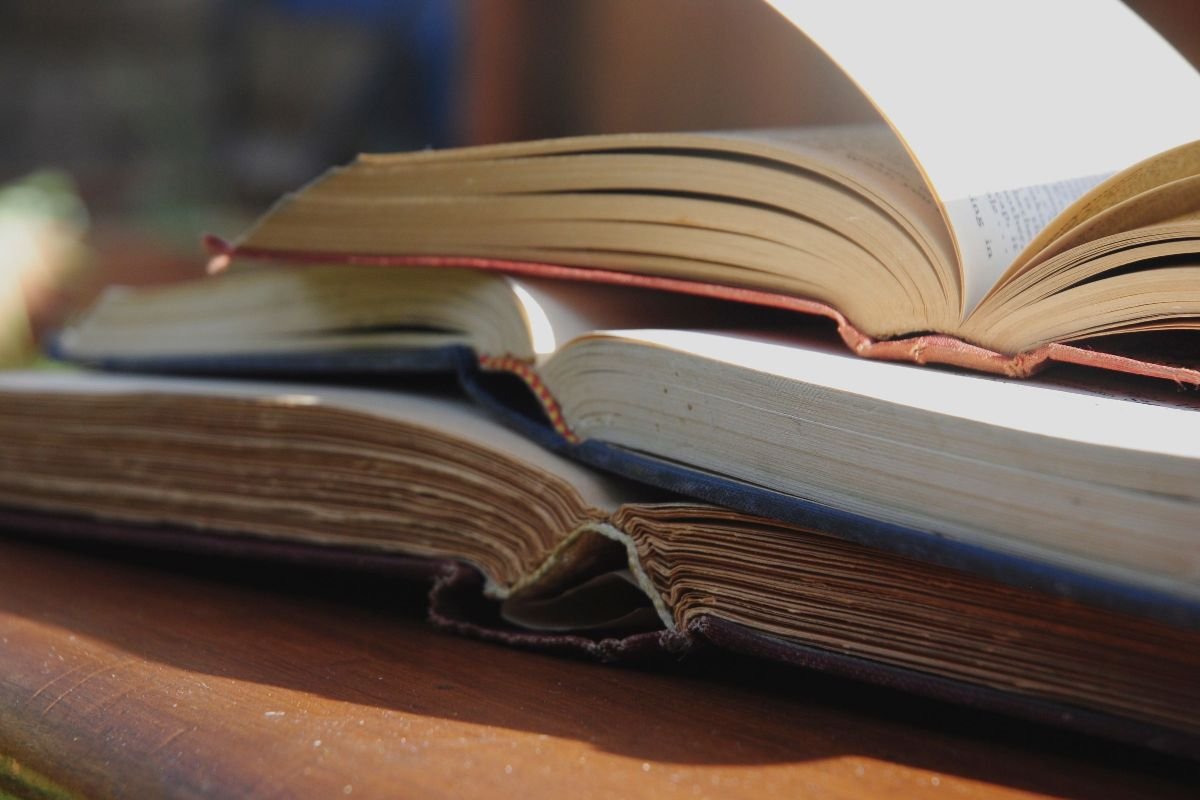 Stack of open books on a sunlit table, representing confidence book notes and summaries
