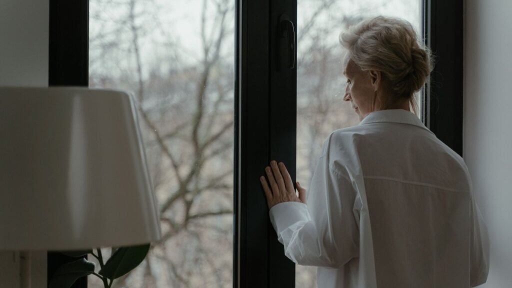 An elderly woman looking thoughtfully through a window