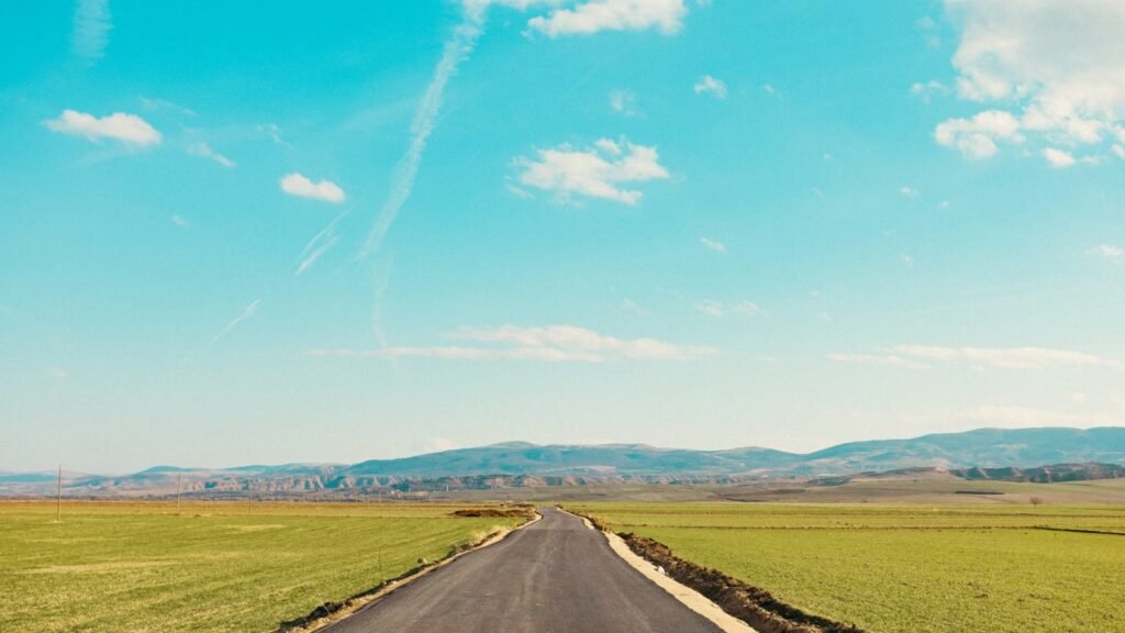 A serene countryside road leading towards distant mountains