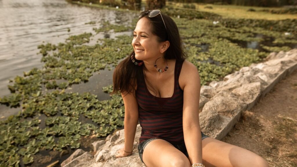 Smiling woman relaxing peacefully by a lake, representing calm and relief