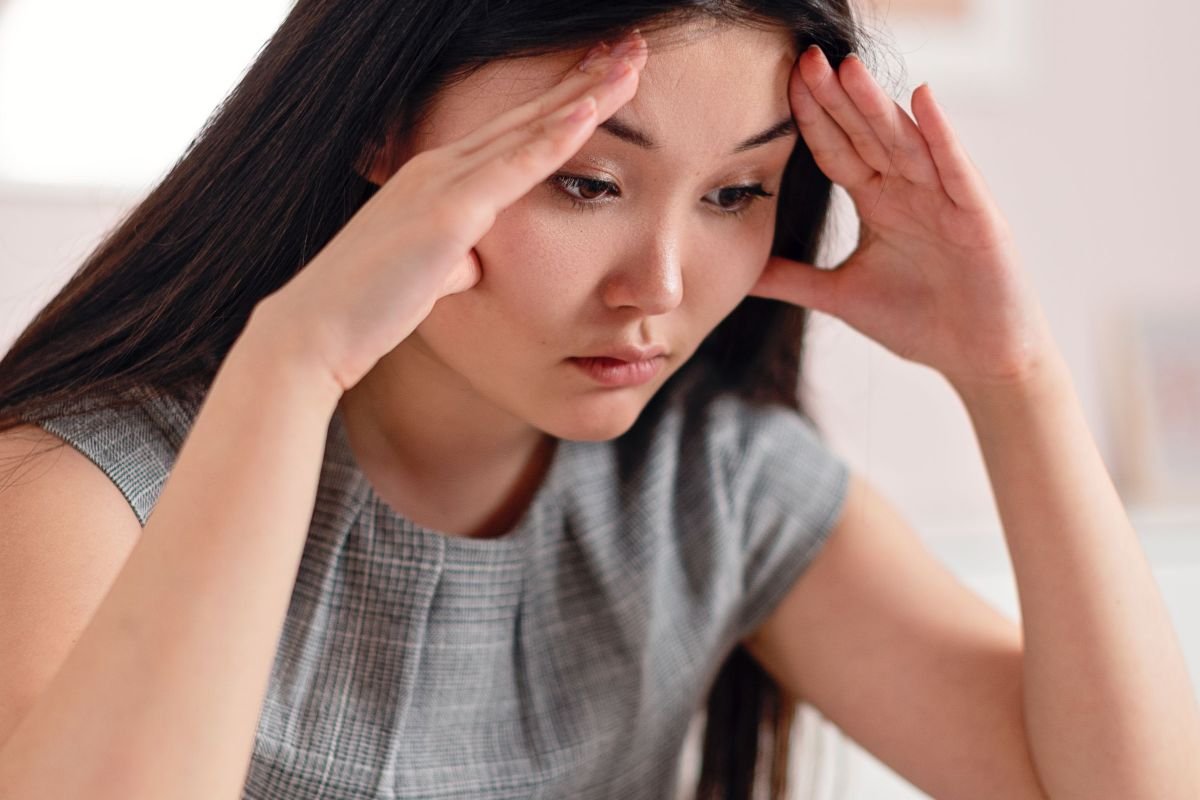 Stressed woman sitting with her hands on her head, overwhelmed by negative thoughts