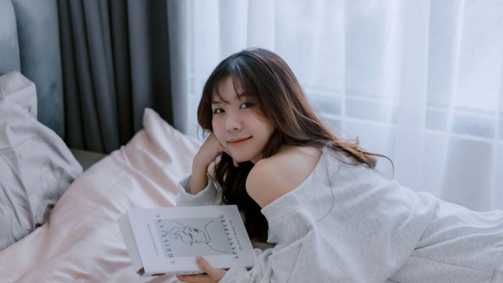 Young woman relaxing on bed reading a book in a cozy indoor setting