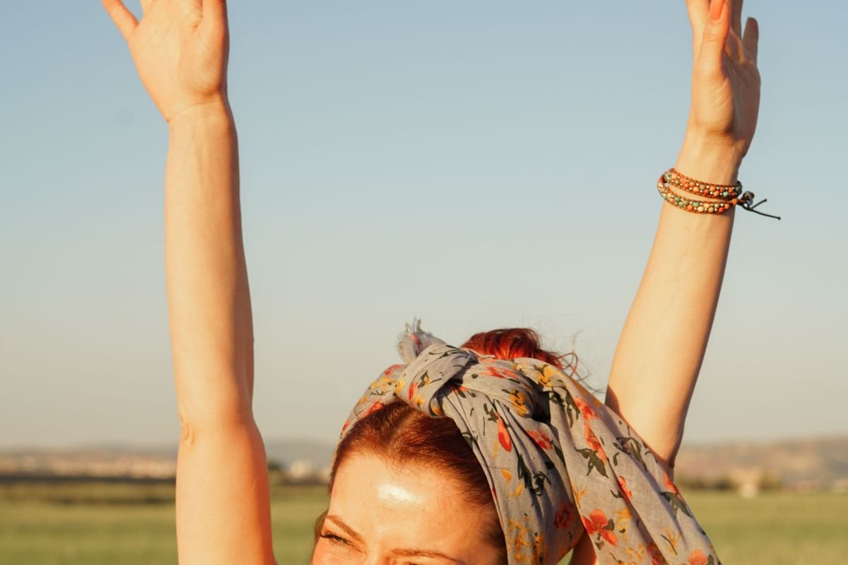 Smiling woman with arms raised joyfully in a sunlit field