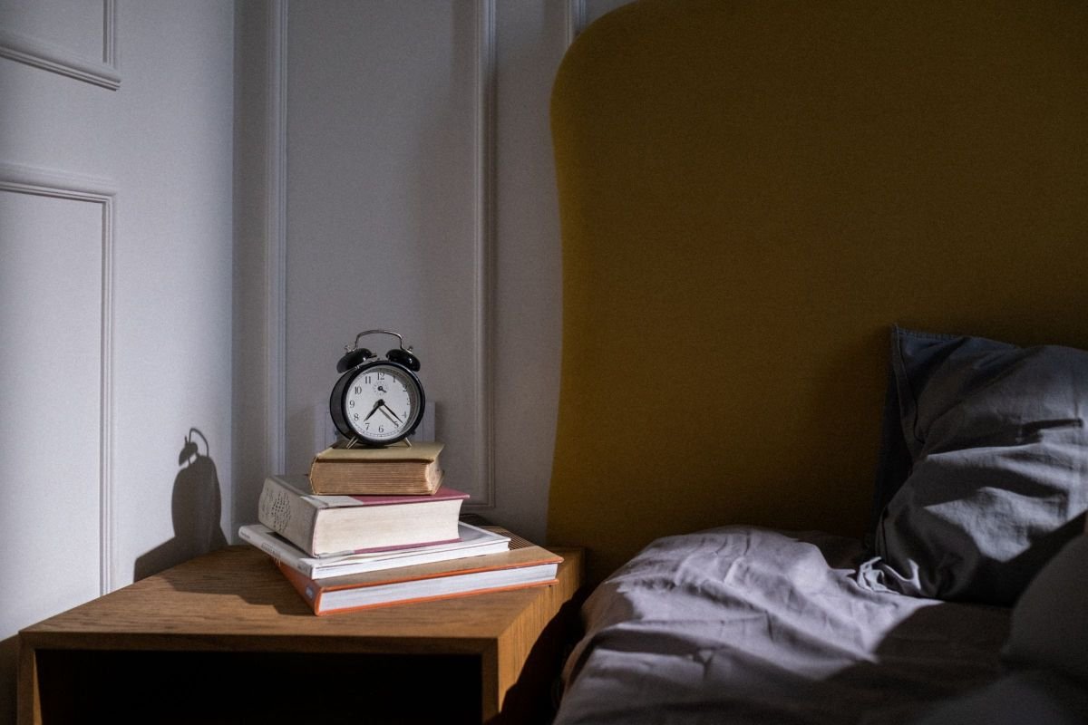 Books and an alarm clock on a nightstand, representing restful time before sleep