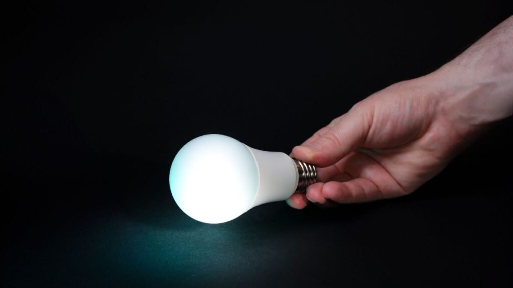 A hand holding a glowing light bulb against a dark background