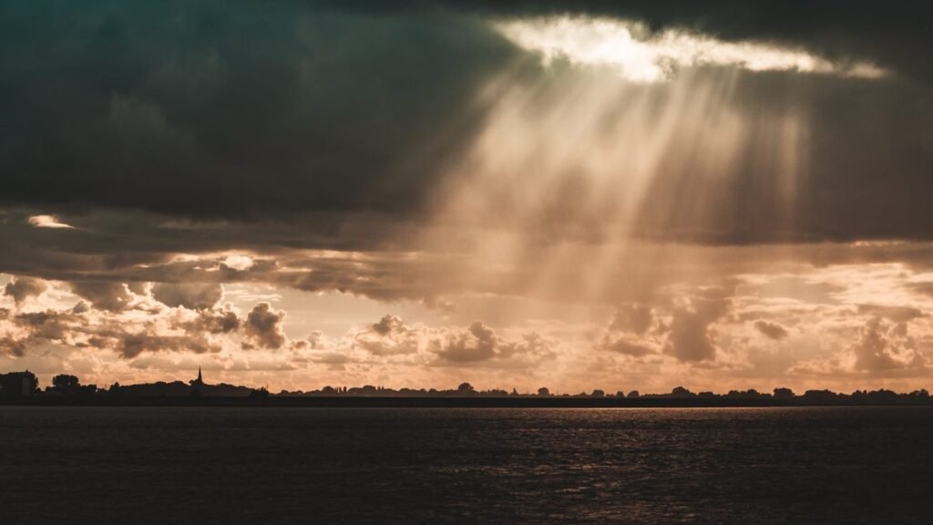 Sun rays breaking dramatically through dark storm clouds over the sea
