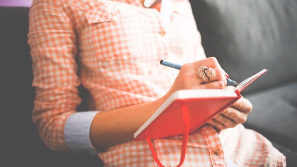 Woman writing in a red journal, reflecting